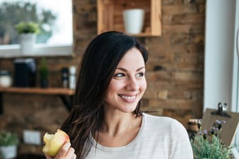 Eine Frau isst einen Apfel und lächelt.