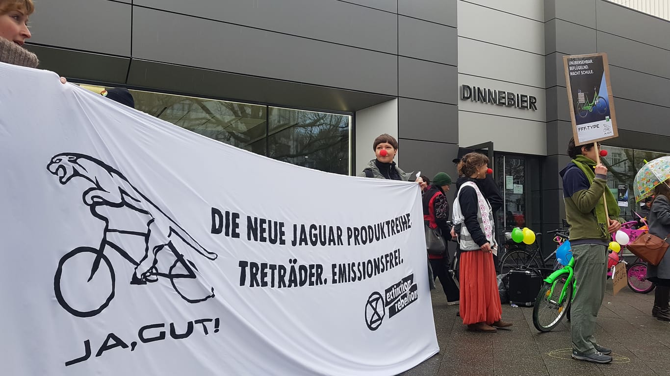 "Die neue Jaguar Produktreihe. Treträder. Emissionsfrei" steht auf einem Transparent, das Aktivisten von "Extinction Rebellion" halten: Sie protestieren vor der Filiale von Jaguar auf dem Kurfürstendamm.