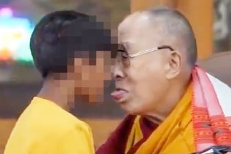 Dalai Lama streckt seine Zunge einem Jungen entgegen