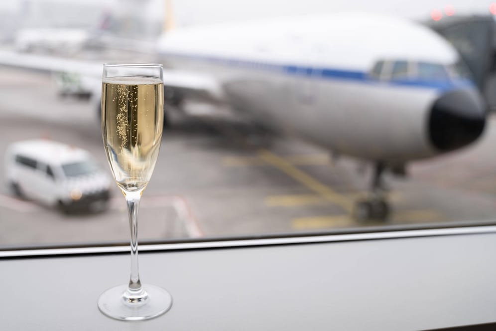 Ein Sektglas vor einem Flugzeug (Symbolbild): Ein Gericht in Hannover wies Forderungen eines Fluggasts zurück.