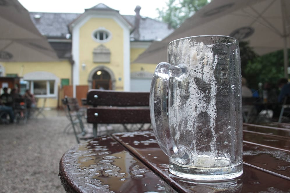 Ein leeres Bierglas auf einem regennassen Tisch in einem Münchner Biergarten (Symbolbild): Am Montag treten Beschäftigte in bayerischen Brauereien in Streik.