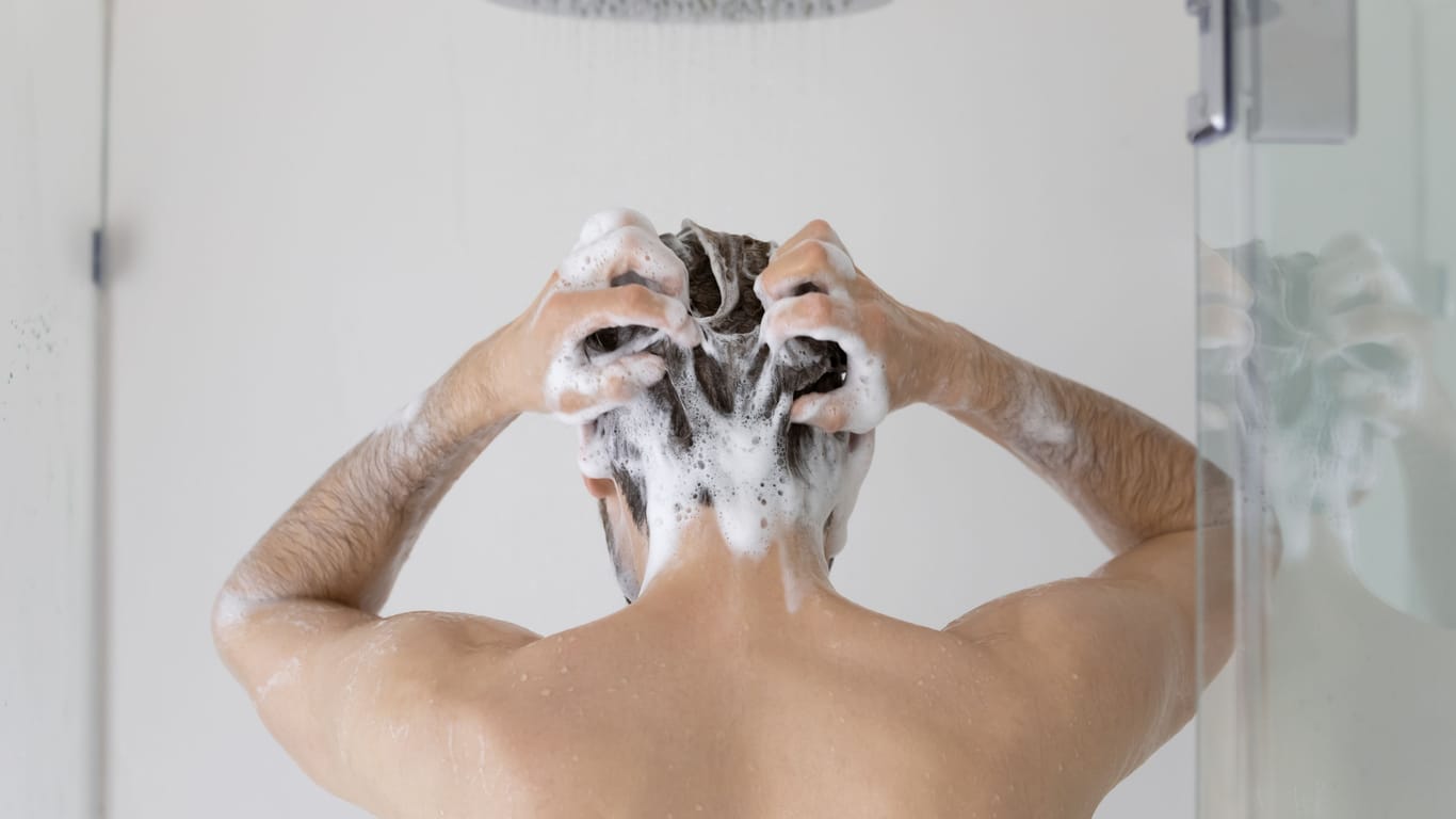 Ein Mann wäscht sich die Haare mit Shampoo.