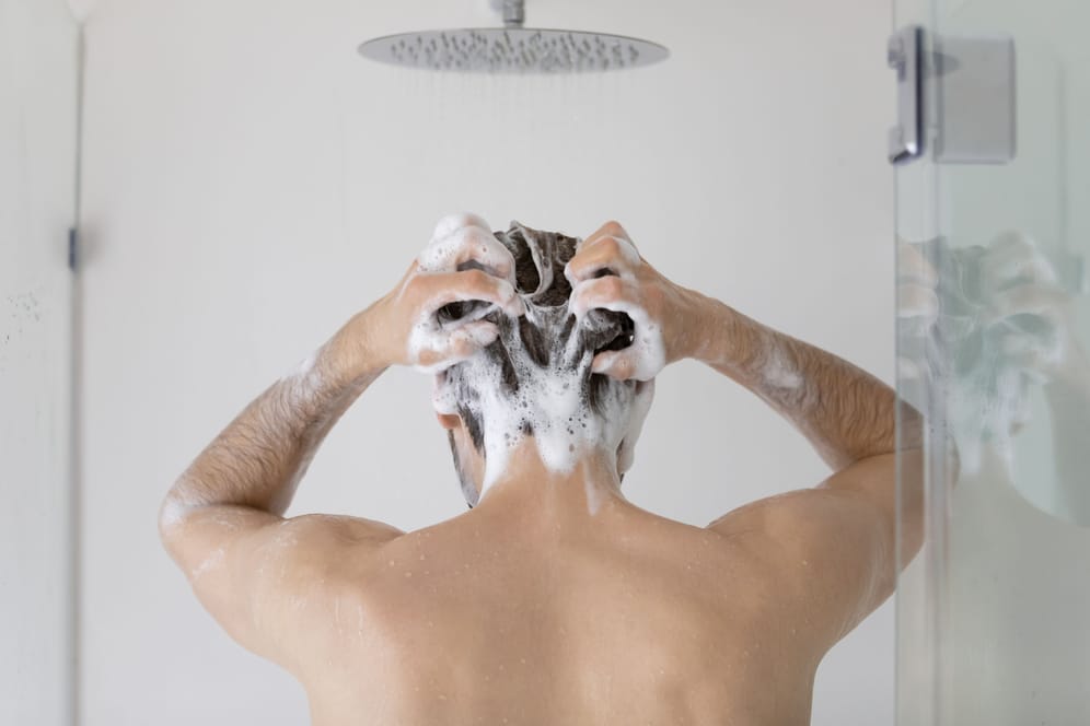 Ein Mann wäscht sich die Haare mit Shampoo.
