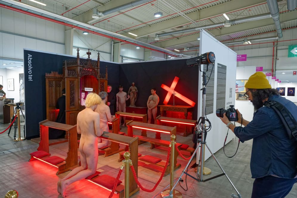 Discovery Art Fair Köln: Nackte Männer und zwei Männer in schwarzen Talaren während einer Kunstaktion.