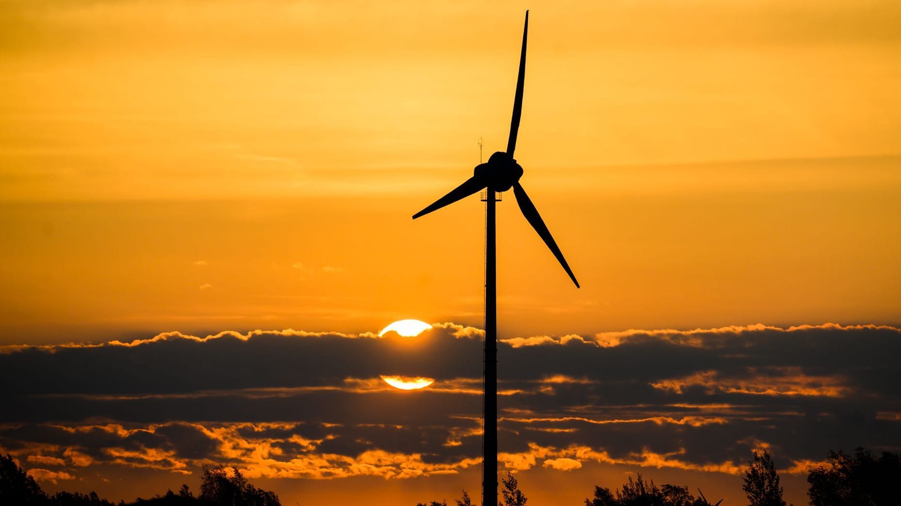 Ein Windrad bei Sonnenaufgang (Symbolfoto): Wechselhaft soll es zugehen rund ums lange Wochenende.