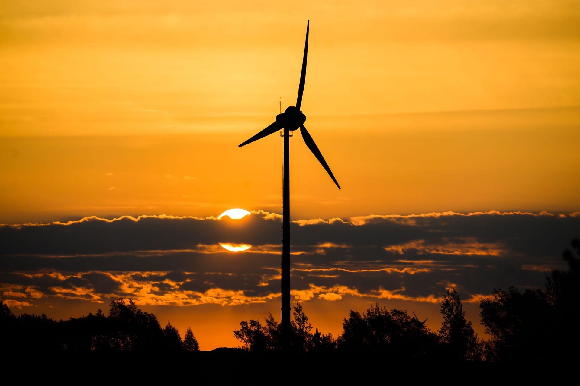 Ein Windrad bei Sonnenaufgang (Symbolfoto): Wechselhaft soll es zugehen rund ums lange Wochenende.