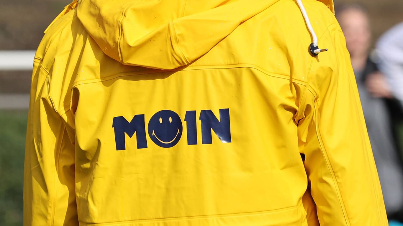 Ein Mann mit gelber Jacke und der Aufschrift "Moin" (Archivfoto): Einmal "Moin" reicht, alles andere verrät Sie nur.