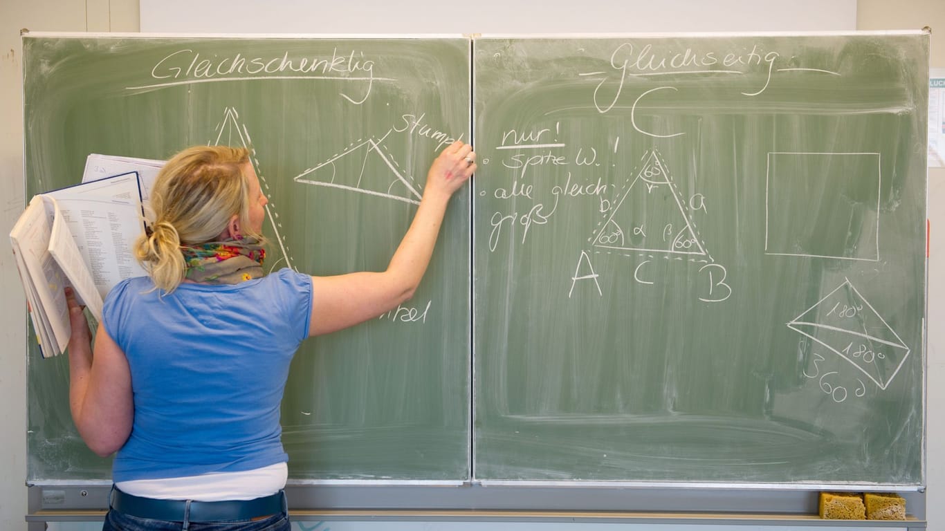 Eine Lehrerin schreibt mit Kreide an eine Tafel (Symbolfoto): Aus der Not heraus, so die GEW, hätten viele Schulen einen "Gemischtwarenladen, was den Fächerkanon angeht".