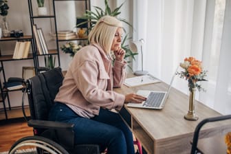 Frau im Rollstuhl arbeitet am Schreibtisch (Symbolbild): Für Menschen mit Schwerbehinderung gelten bei der Altersrente andere Regeln.