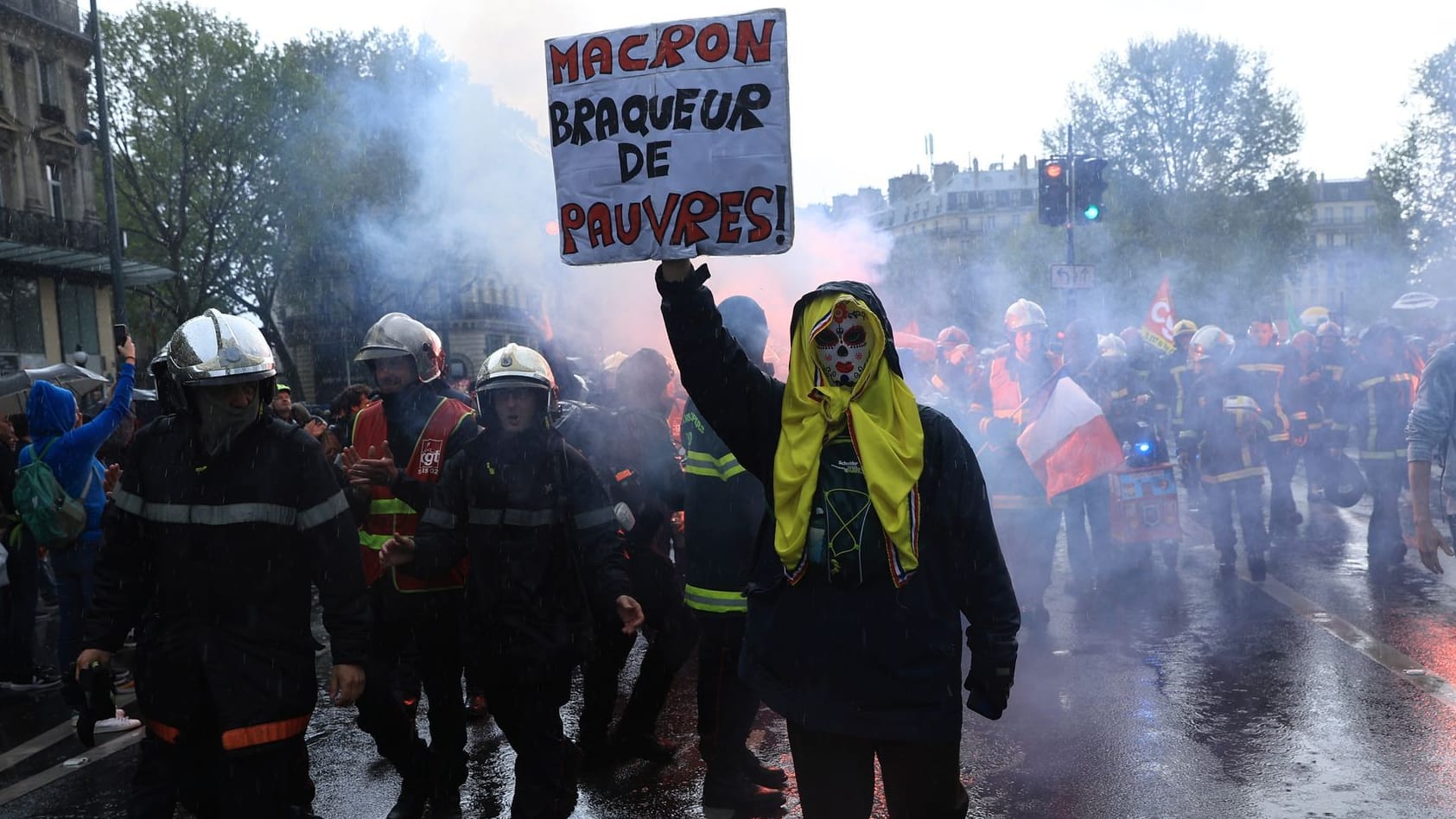 Rettungskräfte und ein Demonstrant mit einem Plakat mit der Aufschrift «Macron, Räuber der Armen» marschieren während einer Demonstration anlässlich des Tages der Arbeit.