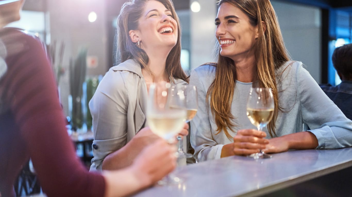Ein paar Frauen sitzen an einer Bar: Wer nach dem Essen länger im Restaurant bleiben möchte, wird in manchen Gegenden an die Bar gebeten, um Tische freizugeben.