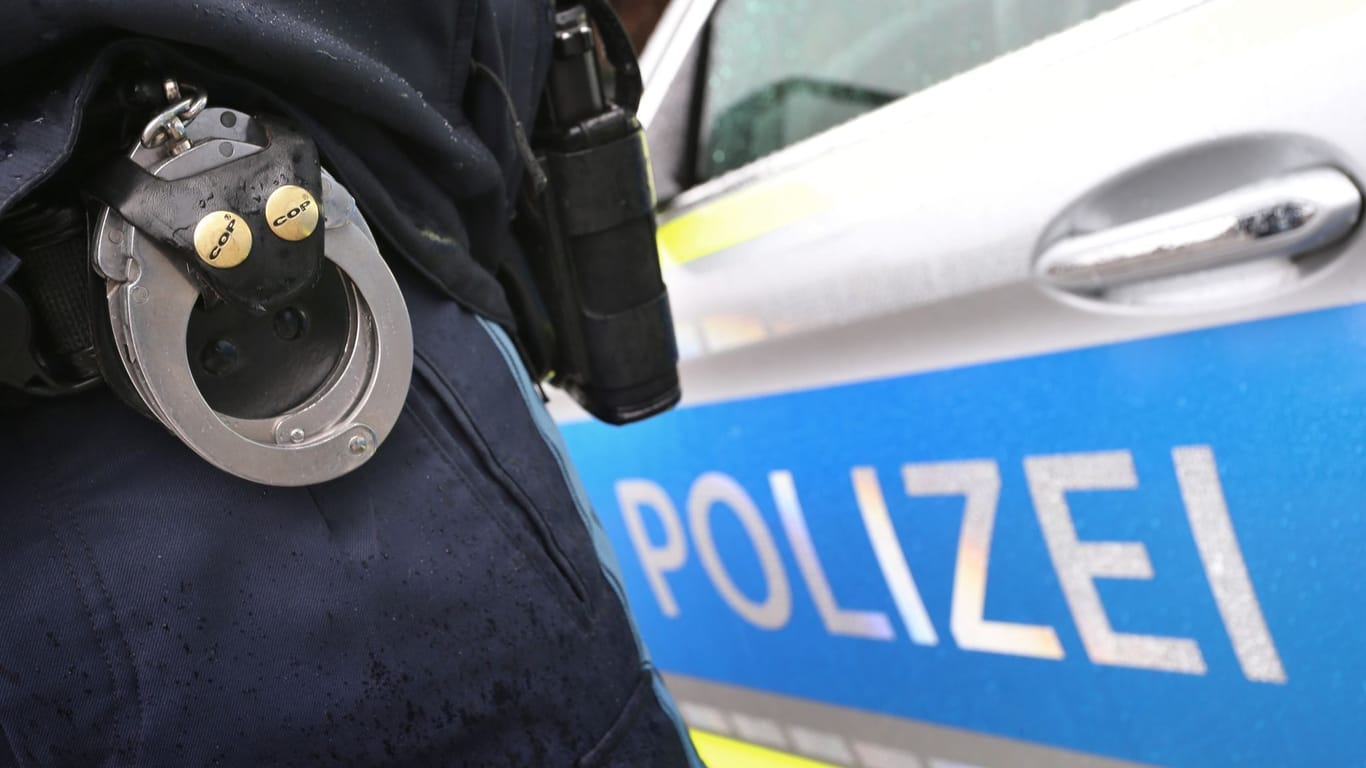 Ein Polizist mit Handschellen und einer Pistole am Gürtel steht vor einem Streifenwagen (Symbolbild): Polizisten mussten am Wochenende zwei Streitende trennen.
