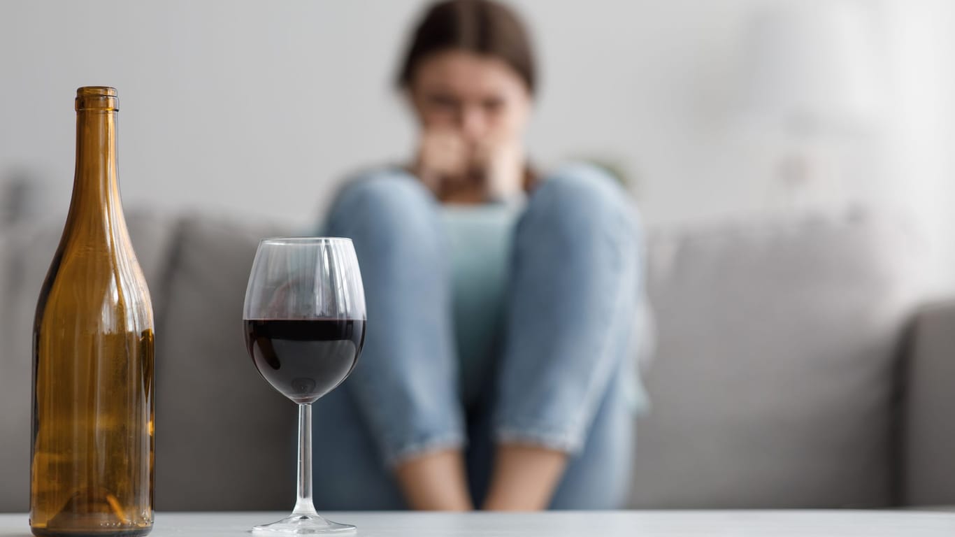 Eine Person sitzt auf einem Sofa, vor ihr ein Glas Rotwein und eine leere Flasche: Alkoholkonsum birgt viele Risiken.