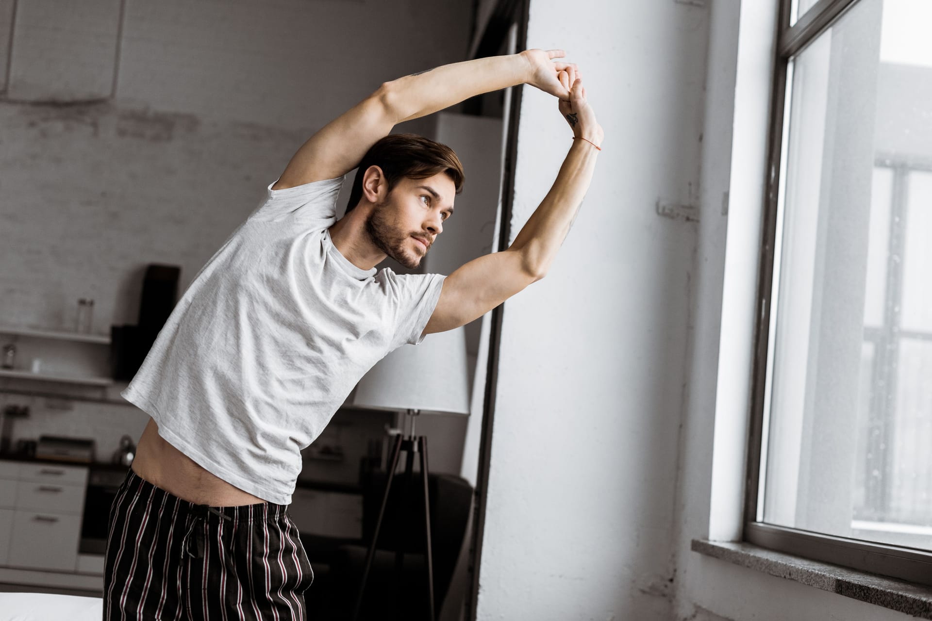 Ein Mann führt Dehnübungen durch und schaut aus dem Fenster.