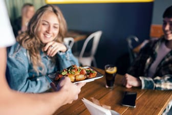 Ein Kellner bringt Essen an einen Tisch: Immer mehr Restaurants geben ein Zeitfenster für den Besuch vor.