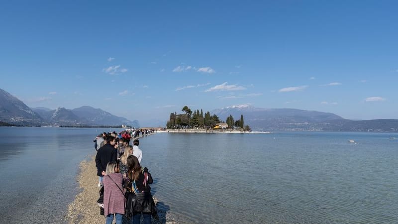 Italien, Gardasee: Menschen spazieren von Punta Belvedere nach Isola dei Conigli über den Gardasee aufgrund des ungewöhnlich niedrigen Wasserstands.