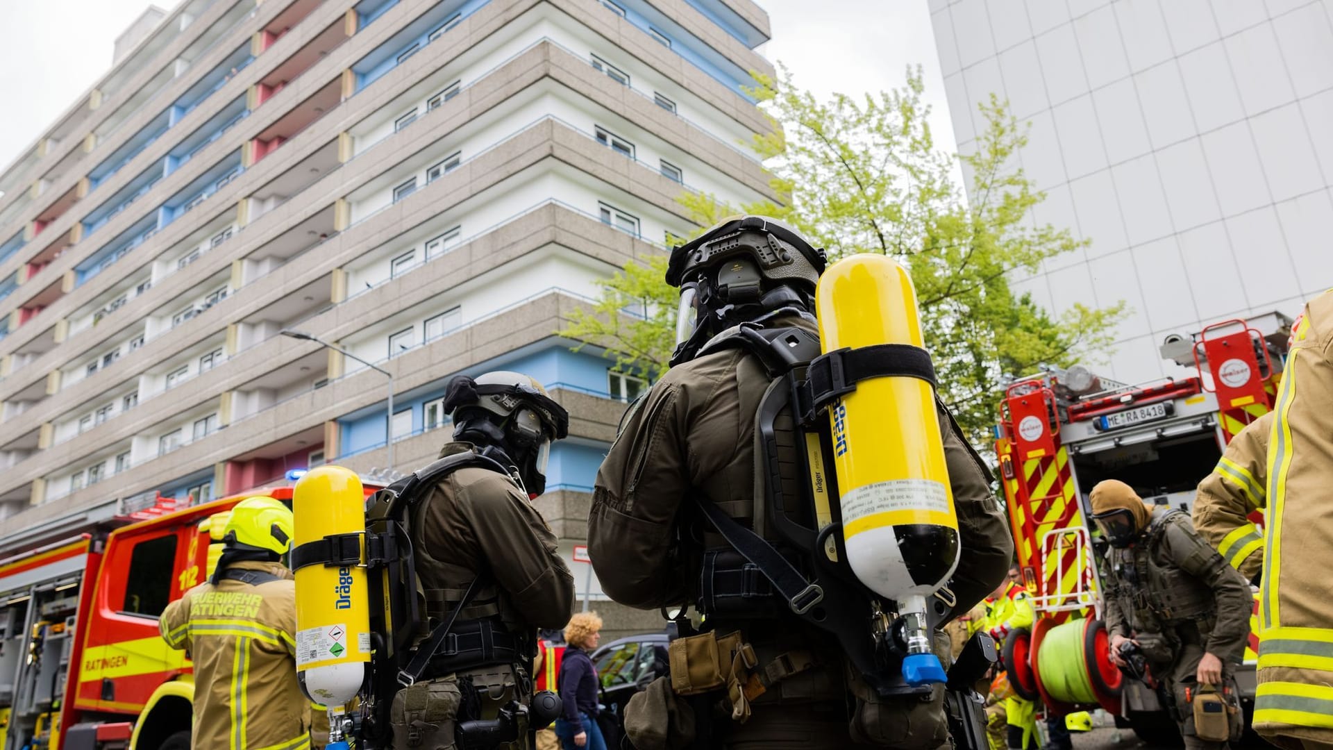 Ratingen: Polizeibeamte mit Gasmasken und Feuerwehrleute stehen vor einem Hochhaus.