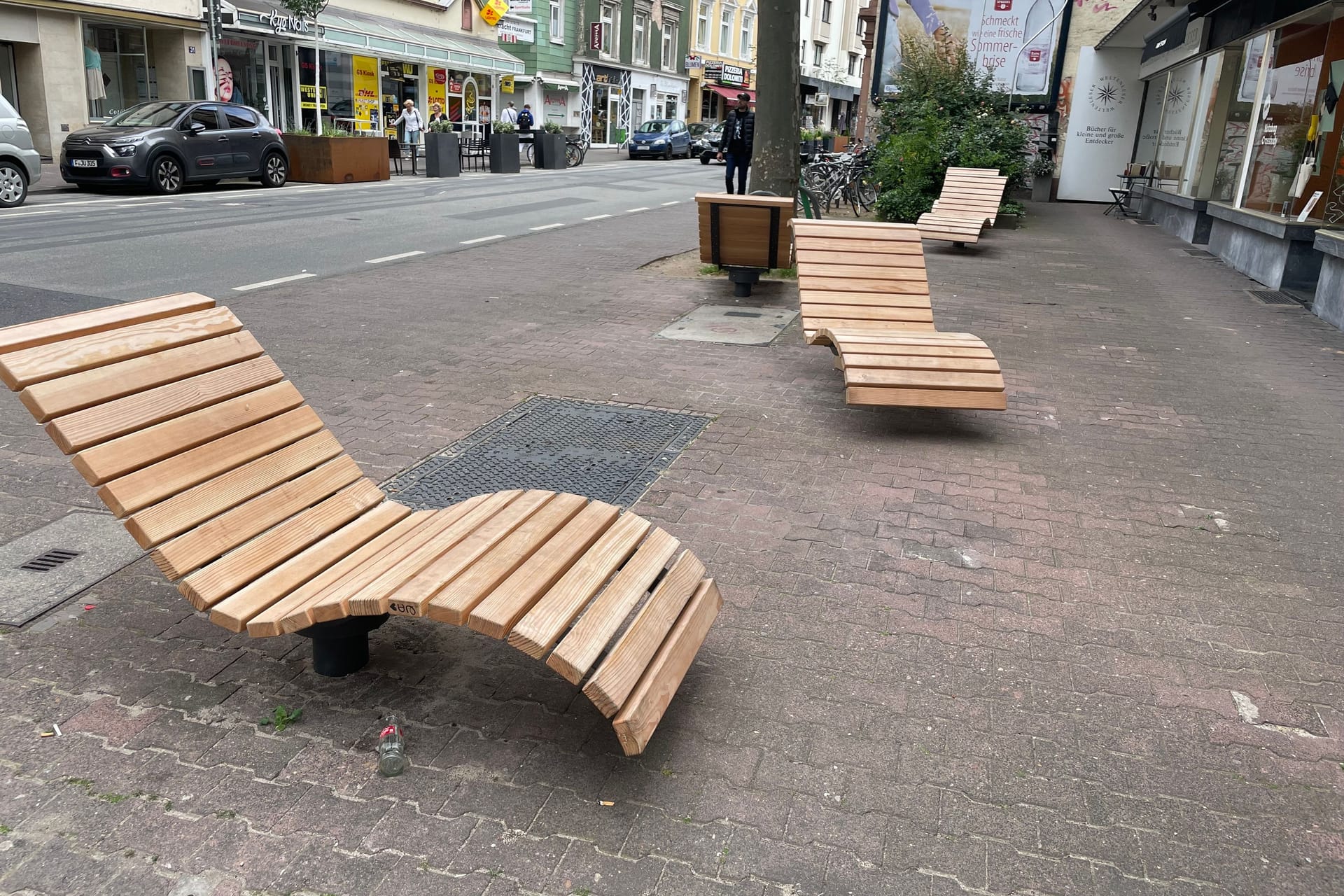 Die Sitzflächen am Oeder Weg. Auf der anderen Straßenseite stehen Pflanzentröge und Tische einer Bäckerei.