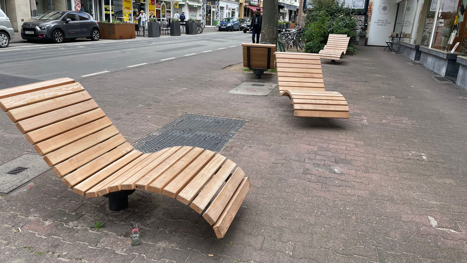 Die Sitzflächen am Oeder Weg. Auf der anderen Straßenseite stehen Pflanzentröge und Tische einer Bäckerei.