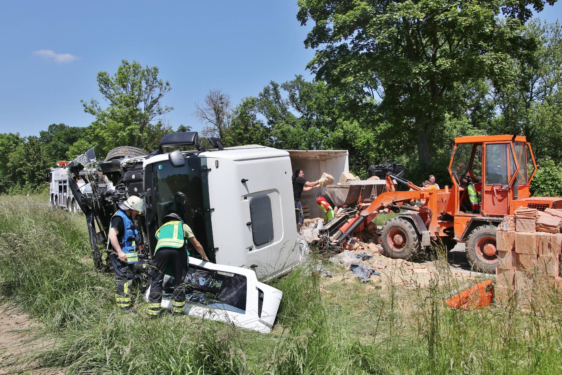 Der Lkw ist auf die Seite gekippt, Helfer räumen die geladenen Ziegelsteine weg: Die Polizei schätzt den Schaden auf rund 90.000 Euro.