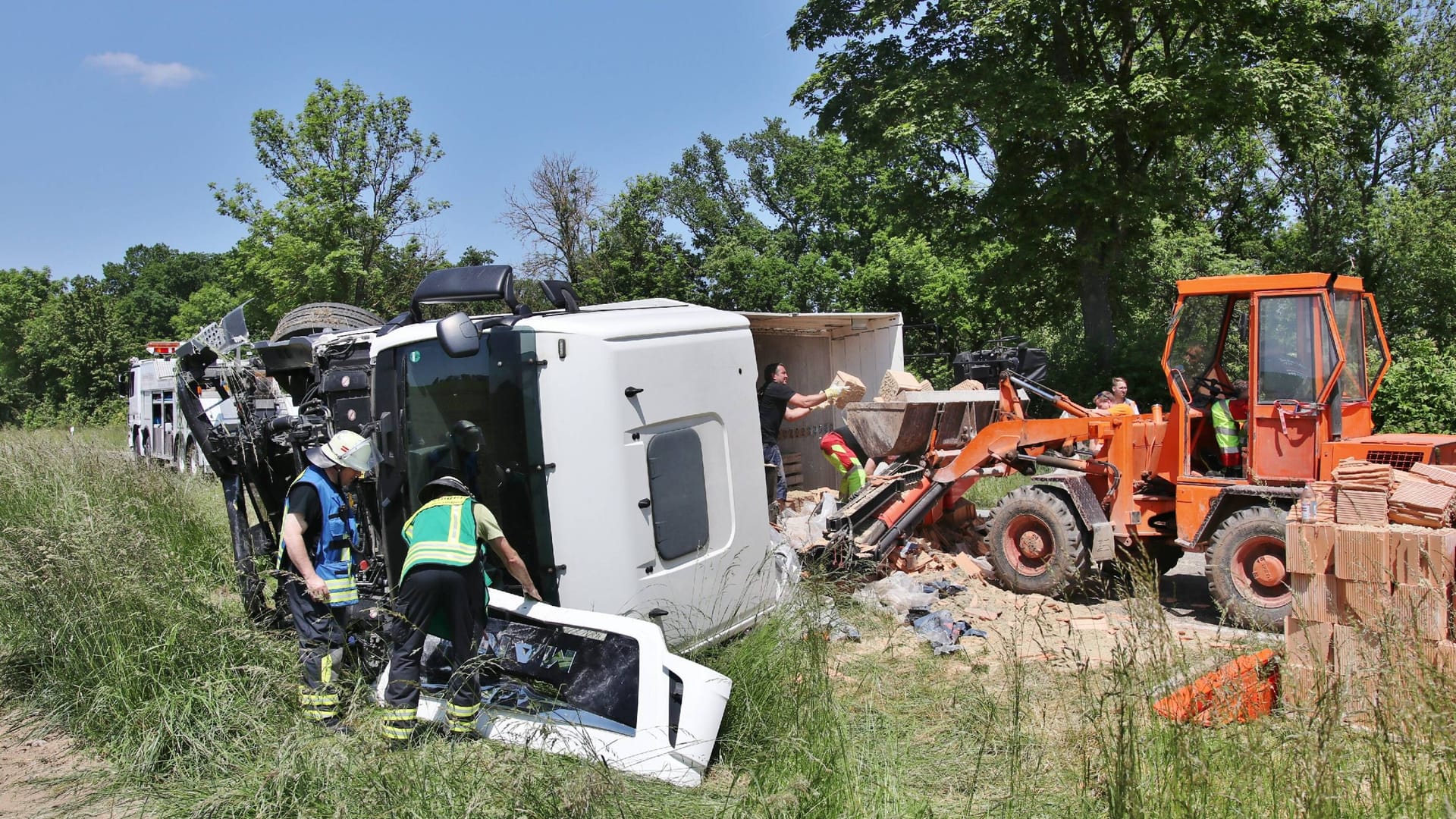 Der Lkw ist auf die Seite gekippt, Helfer räumen die geladenen Ziegelsteine weg: Die Polizei schätzt den Schaden auf rund 90.000 Euro.