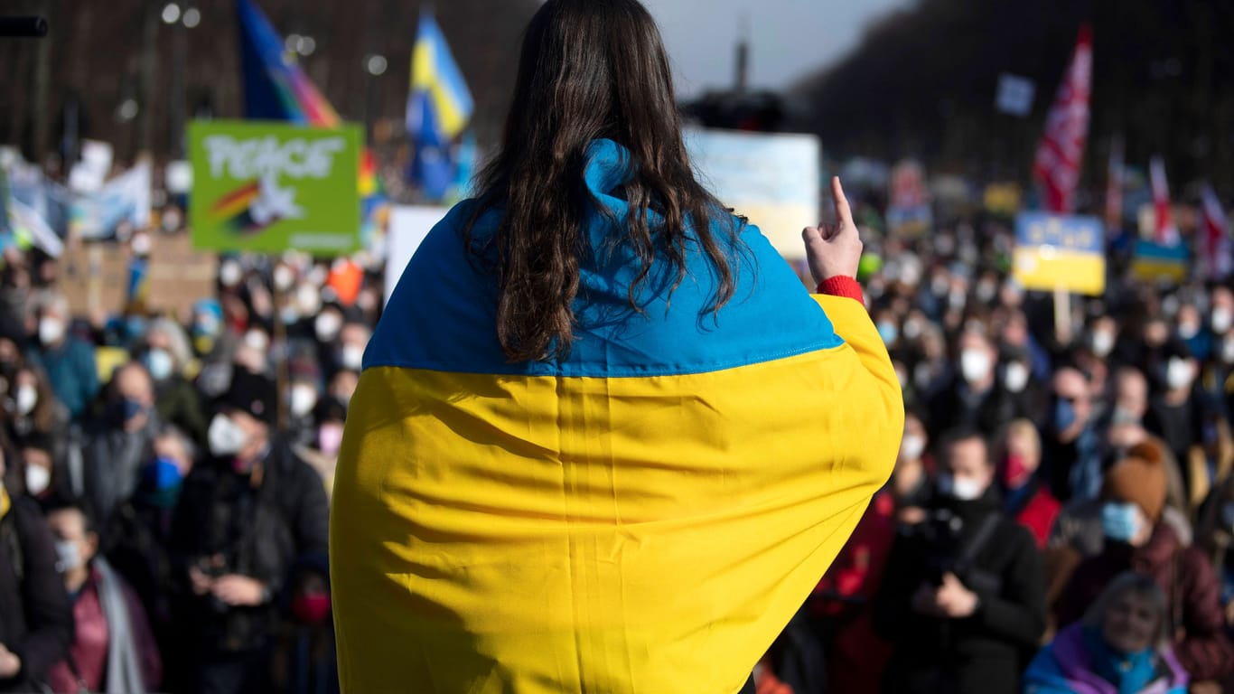 Eine Frau ist in eine Ukraine-Flagge gewickelt: An mehreren Orten in Berlin werden ukrainische und russische Symbole verboten.