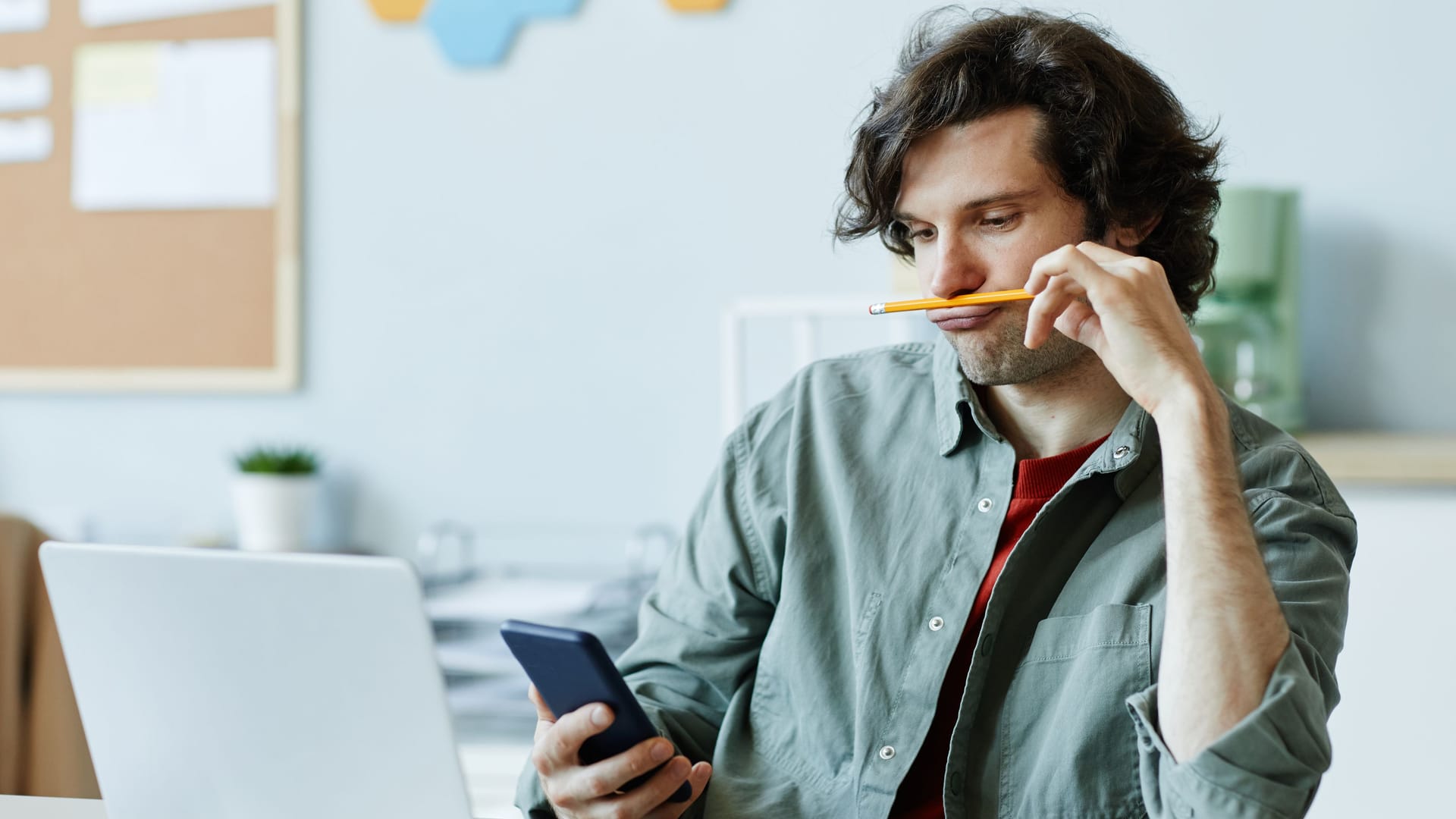 Junger Mann am Laptop schaut auf sein Smartphone