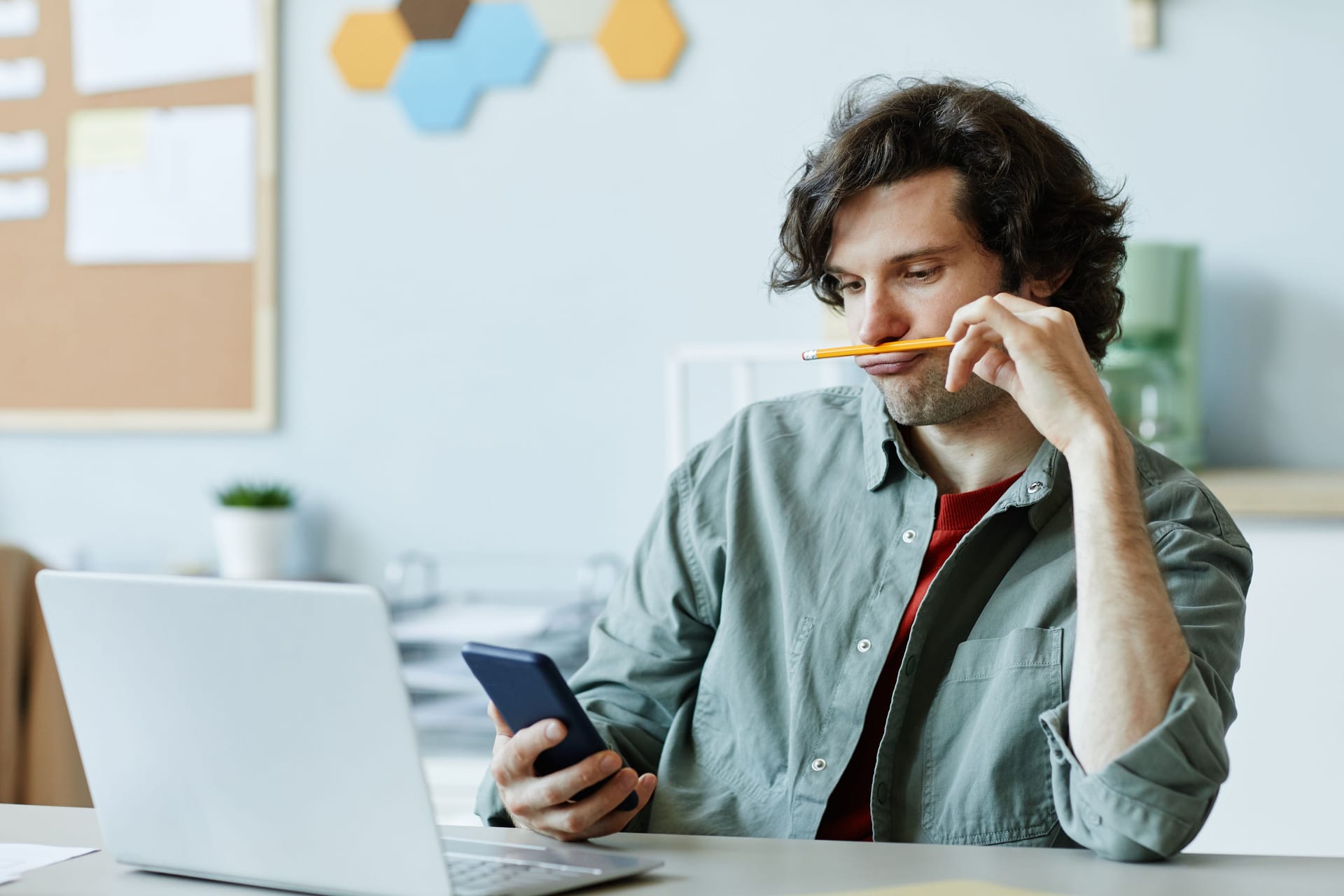 Junger Mann am Laptop schaut auf sein Smartphone