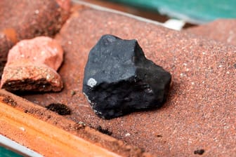Kleiner schwarzer Meteorit auf einer zerbrochenen Dachpfanne: Er hatte ein Dach in Elmshorn durchschlagen.