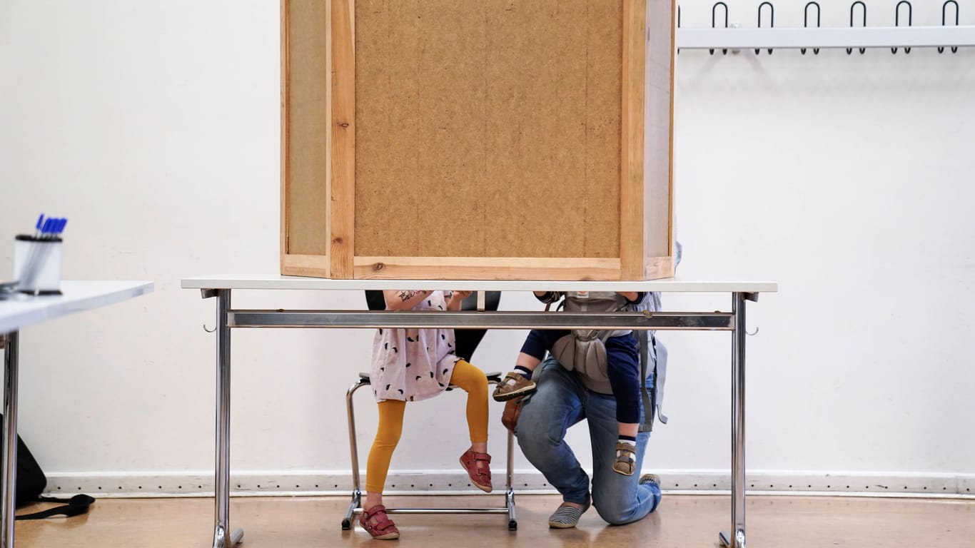 Mutter mit Kindern in Wahlurne (Symbolbild): Ab der kommenden Wahl 2026 sollen 16-Jährige mitentscheiden dürfen.