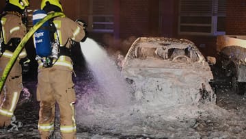 Ein Feuerwehrmann steht in Moabit an einem zerstörten Auto und löscht nach: Das Fahrzeug war aus bislang ungeklärten Ursachen in Brand geraten.