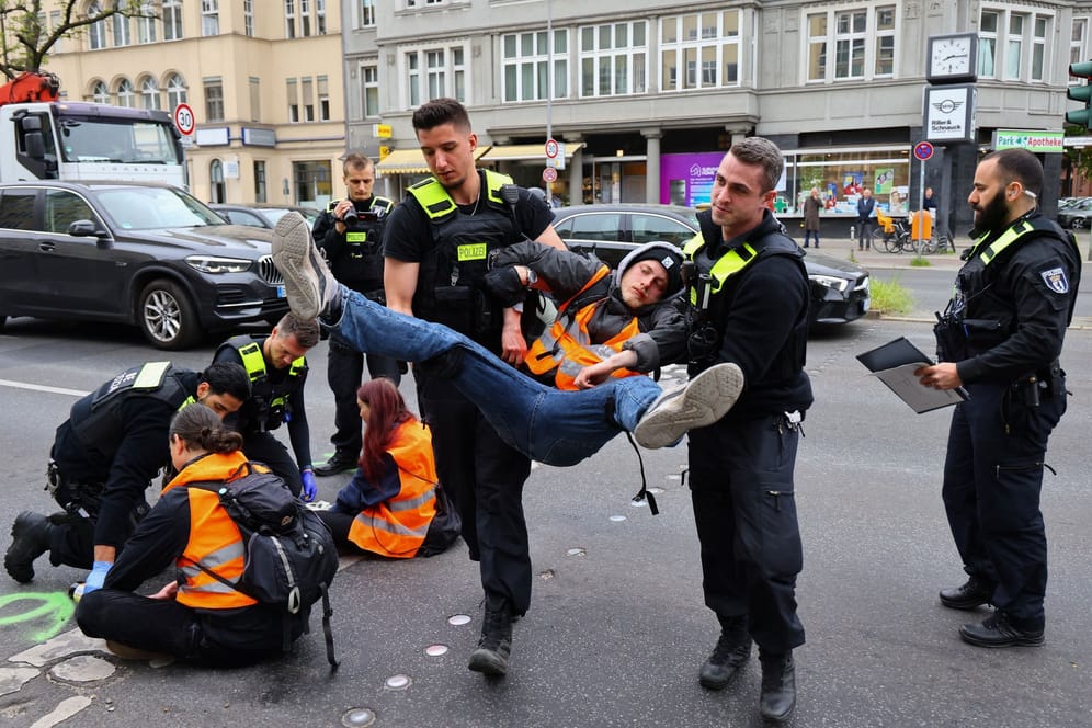 Polizisten tragen einen Mann weg: Er hatte sich in Steglitz zuvor an einen Autoreifen geklebt.