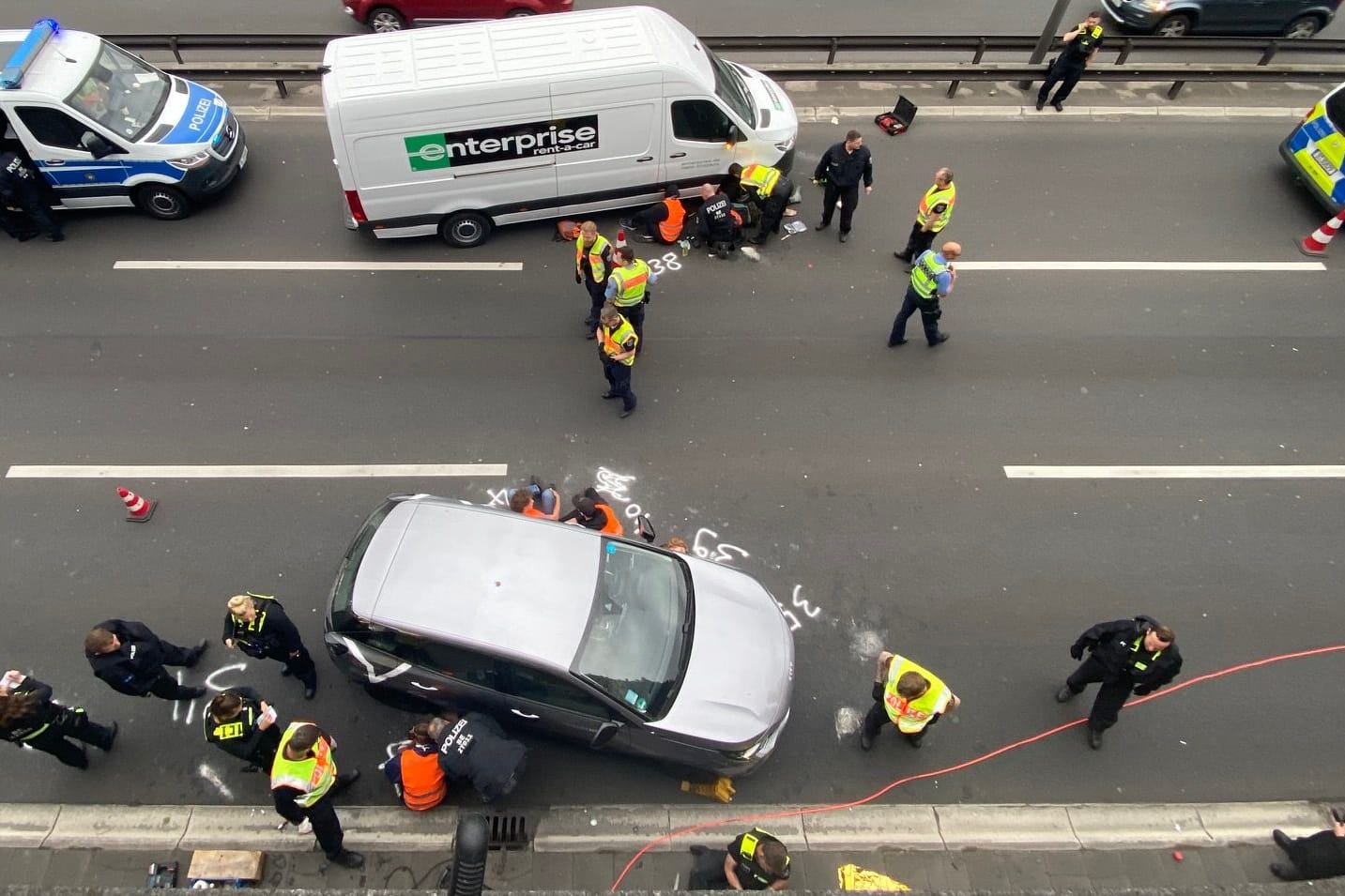 Einsatzkräfte versuchen, die Aktivisten von der Straße loszumachen: Sie haben sich offenbar an Autos festgeklebt.