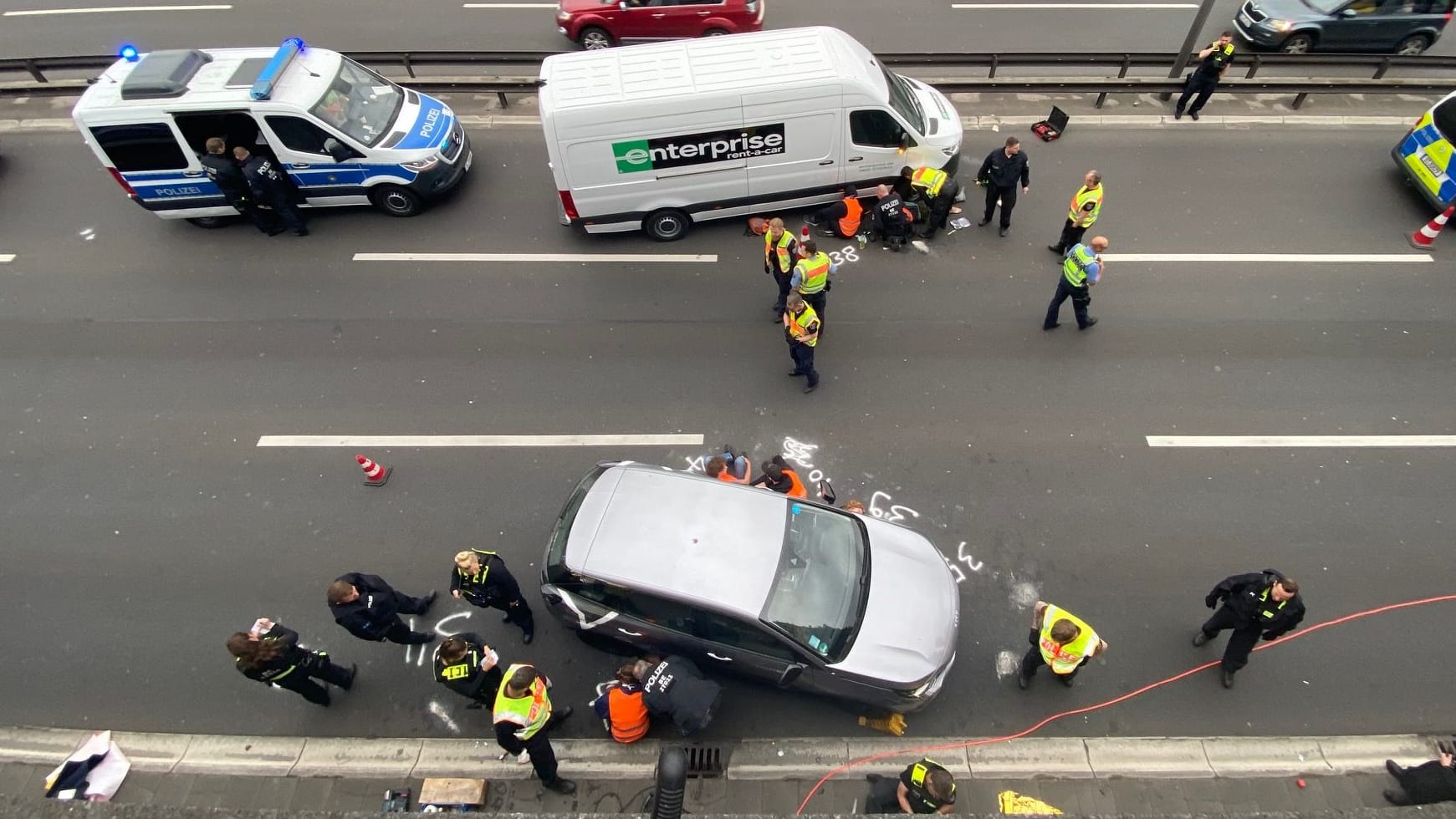 Einsatzkräfte versuchen, die Aktivisten von der Straße loszumachen: Sie haben sich offenbar an Autos festgeklebt.