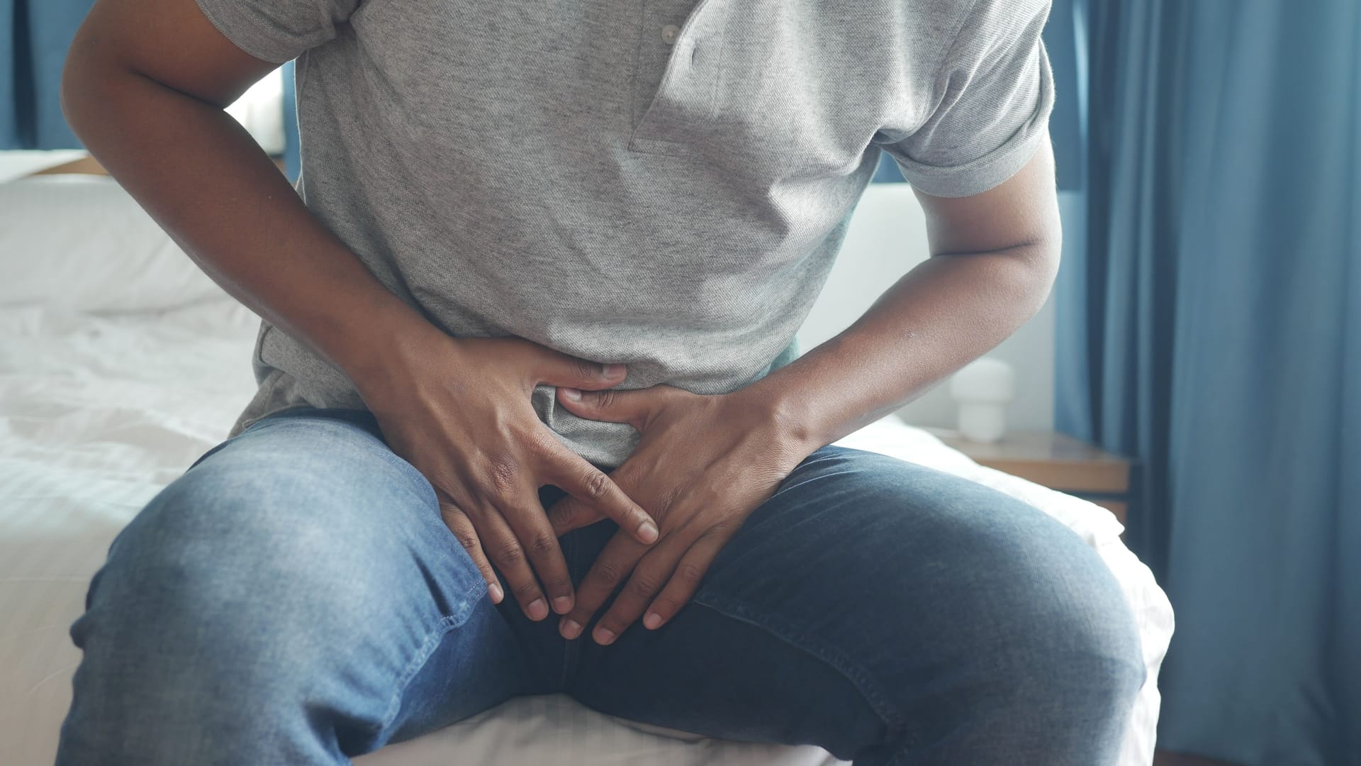 Ein sitzender Mann greift sich in den Schritt: Besteht der Verdacht, dass eine Varikozele die Fruchtbarkeit stört, kann es ratsam sein, die Krampfadern im Hoden zu behandeln.