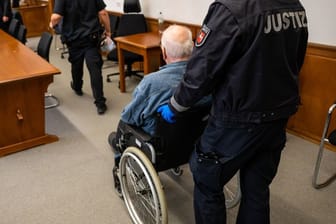 Der Angeklagte wird im Rollstuhl in den Saal des Landgerichts geschoben.