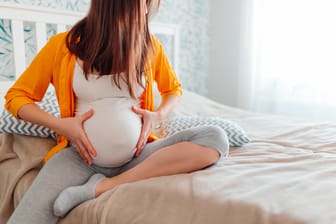 Schwangere Frau sitzt auf dem Bett: In der Schwangerschaft tauchen manchmal Krampfadern an den Schamlippen auf.