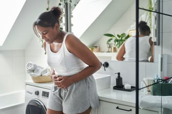 Junge Frau mit Bauchschmerzen und Übelkeit im Bad: Ist das Wetter länger heiß, kommt es unter Umständen öfter zu Magen-Darm-Beschwerden.