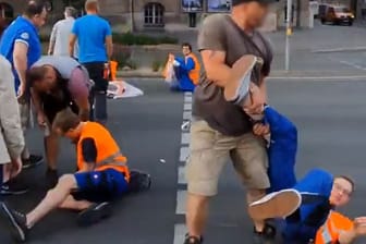 Blockade in Nürnberg: Ein Mann zerrt einen Aktivisten der "Letzten Generation" am Bein von der Straße.