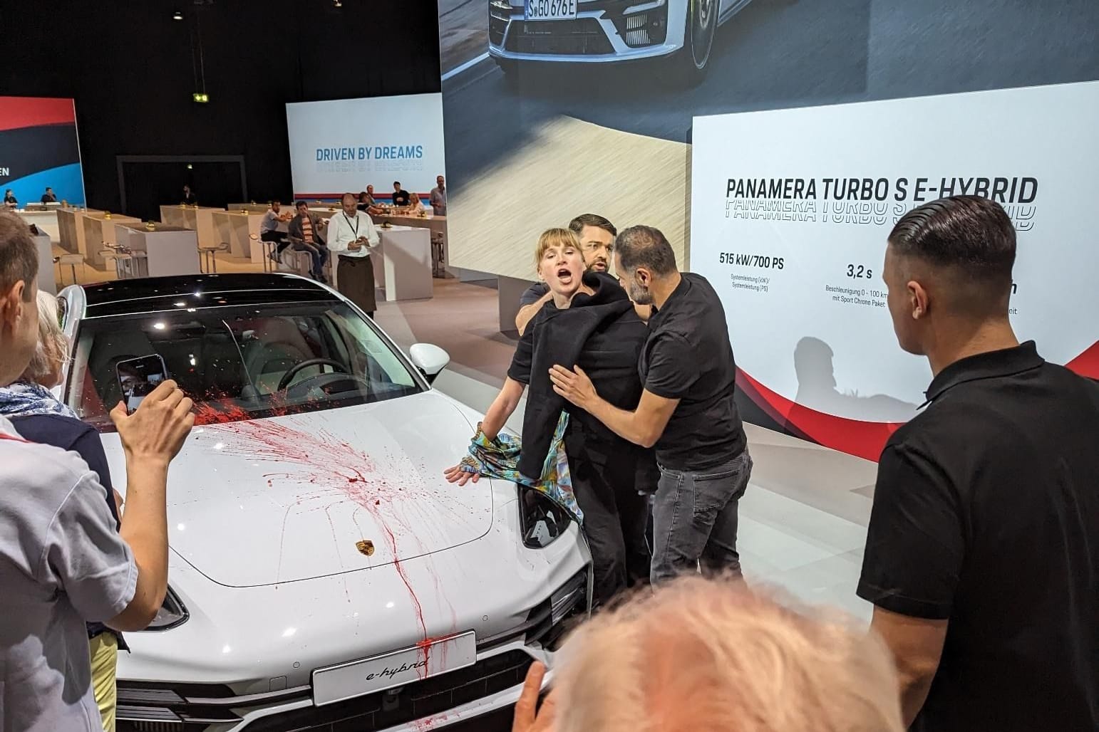 Protest in der Stuttgarter Porsche Arena: Eine Aktivistin hat sich mit entblößter Brust an einen Porsche geklebt. Zuvor beschmierte sie das ausgestellte Fahrzeug.