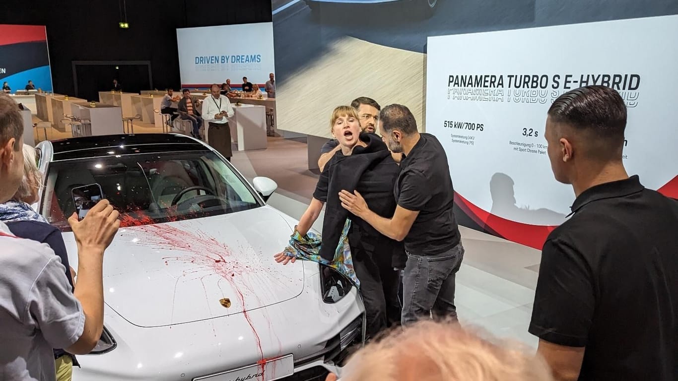 Protest in der Stuttgarter Porsche Arena: Eine Aktivistin hat sich mit entblößter Brust an einen Porsche geklebt. Zuvor beschmierte sie das ausgestellte Fahrzeug.
