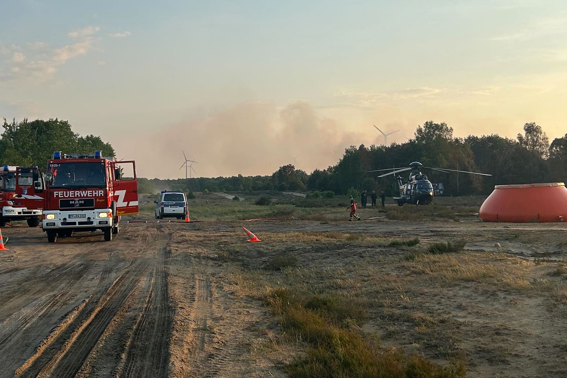 Feuerwehrkräfte sind neben einem Löschhubschrauber in einem Waldstück nahe Jüterbog im Einsatz.