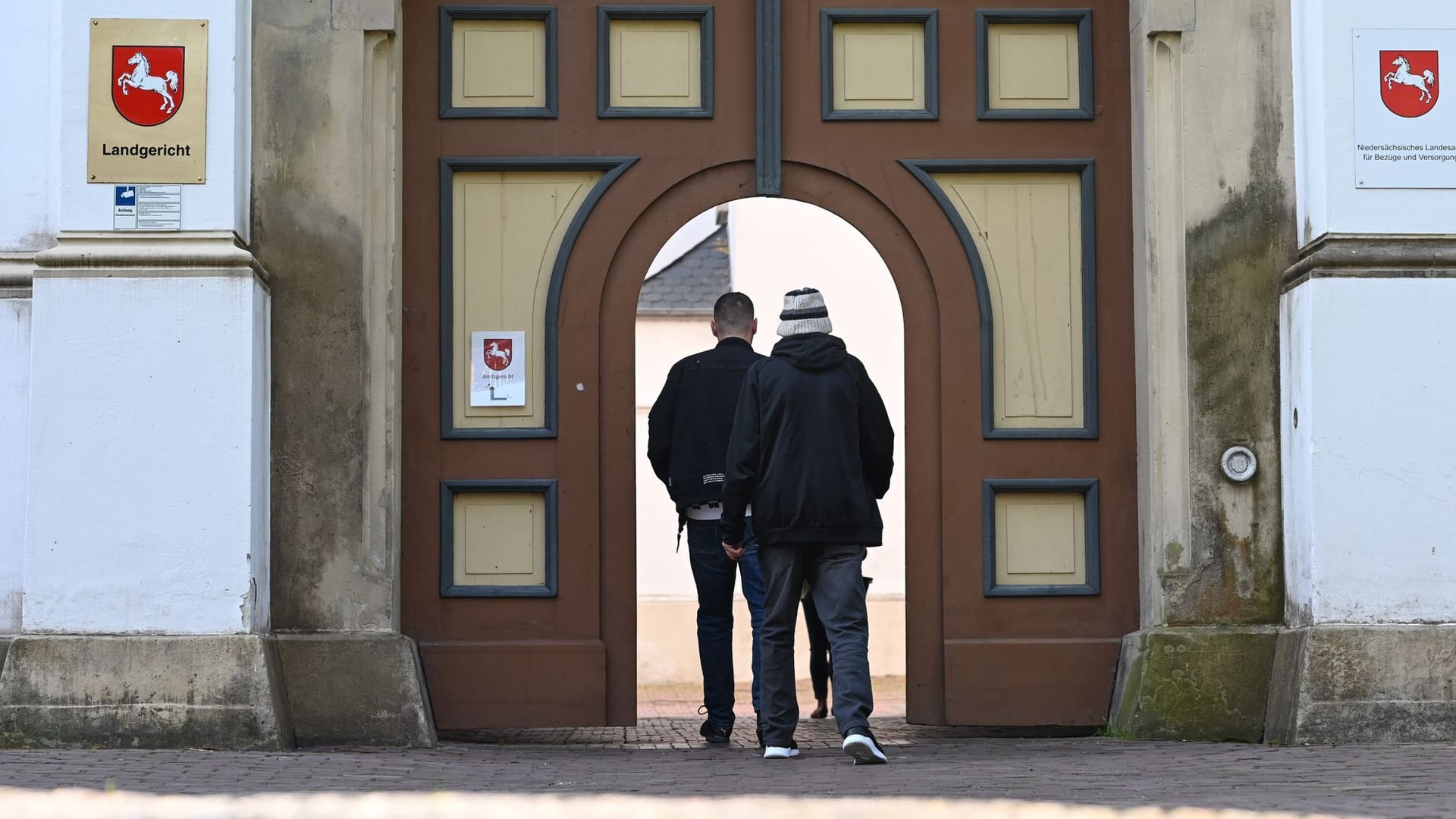 Der Angeklagte (r) betritt den Haupteingang zum Landgericht Aurich.