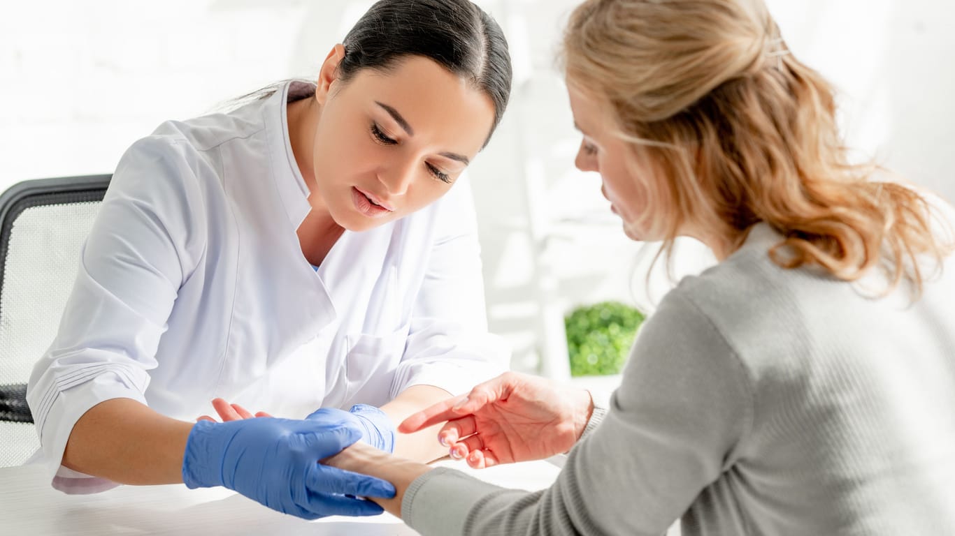 Hautärztin untersucht das Handgelenk einer Frau