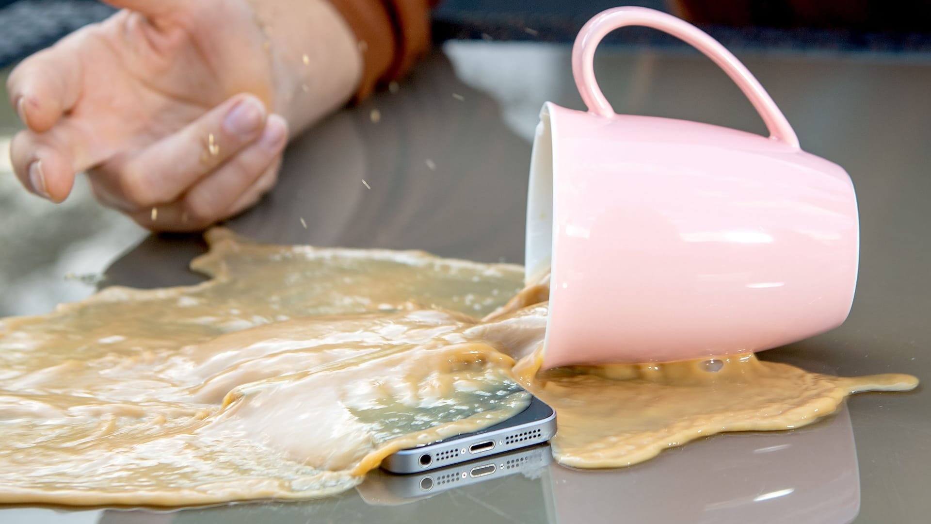 Kaffee ergießt sich über ein Smartphone (Symbolbild): Eine Haftpflichtversicherung springt ein, wenn Sie Dritten einen Schaden zufügen.