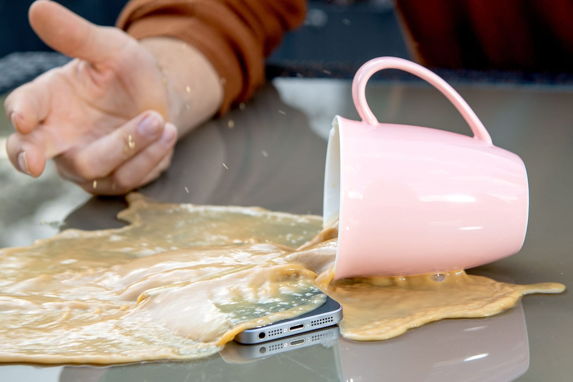 Kaffee ergießt sich über ein Smartphone (Symbolbild): Eine Haftpflichtversicherung springt ein, wenn Sie Dritten einen Schaden zufügen.