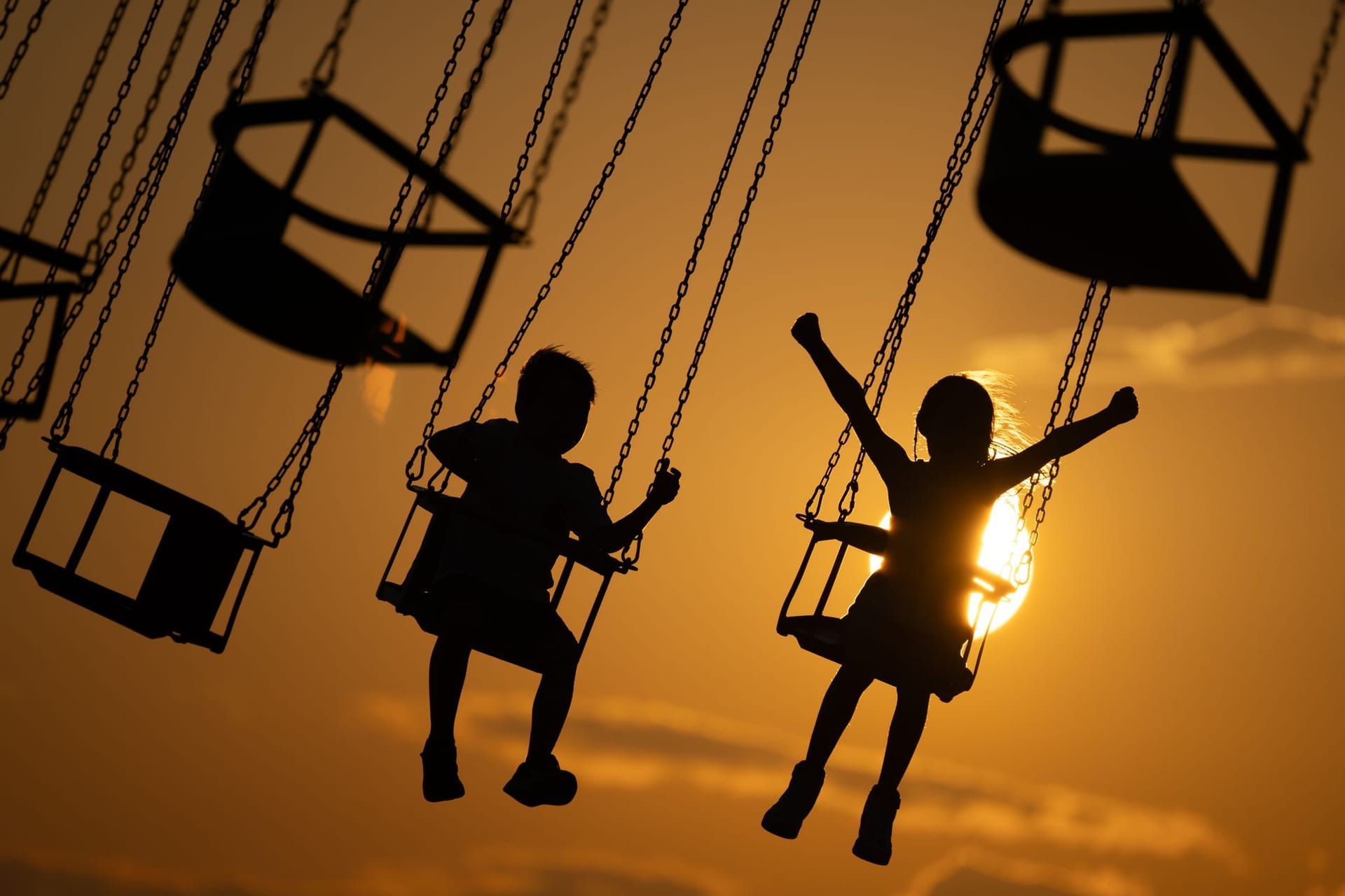 Kinder in einem Kettenkarussell bei Sonnenuntergang (Symbolfoto): Der Donnerstag zeigt sich noch unbeständig, dann könnte es jedoch wärmer werden.