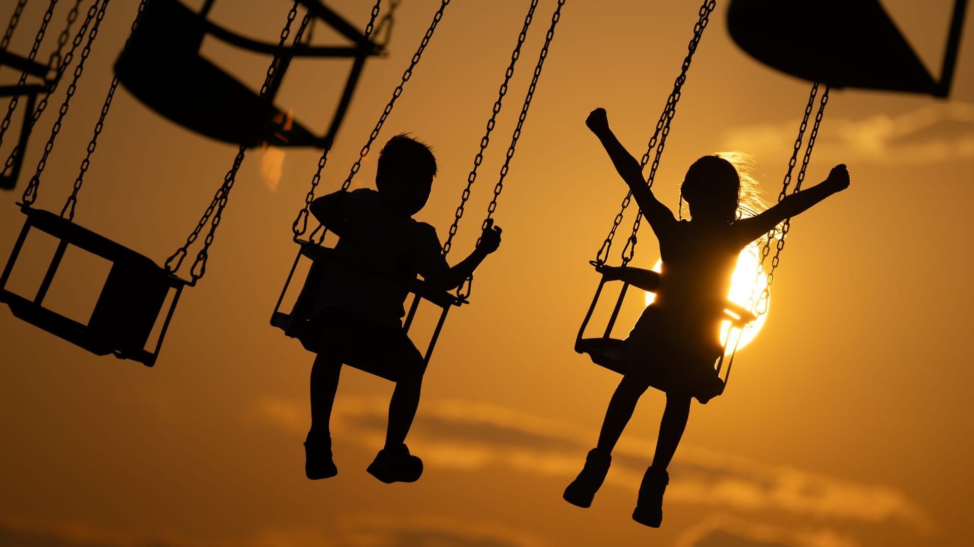 Kinder in einem Kettenkarussell bei Sonnenuntergang (Symbolfoto): Der Donnerstag zeigt sich noch unbeständig, dann könnte es jedoch wärmer werden.