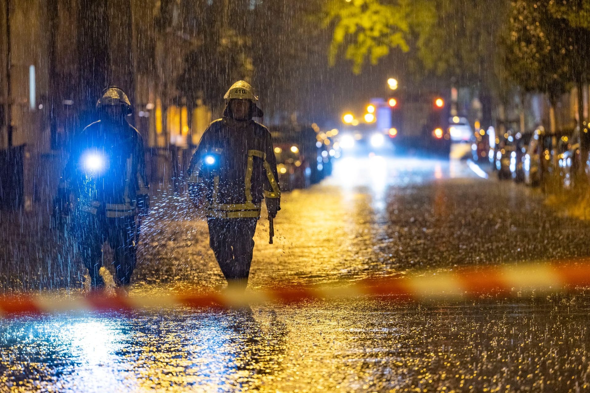 Feuerwehrleute suchen auf einer überfluteten Straße in Duisburg nach Gullydeckeln.