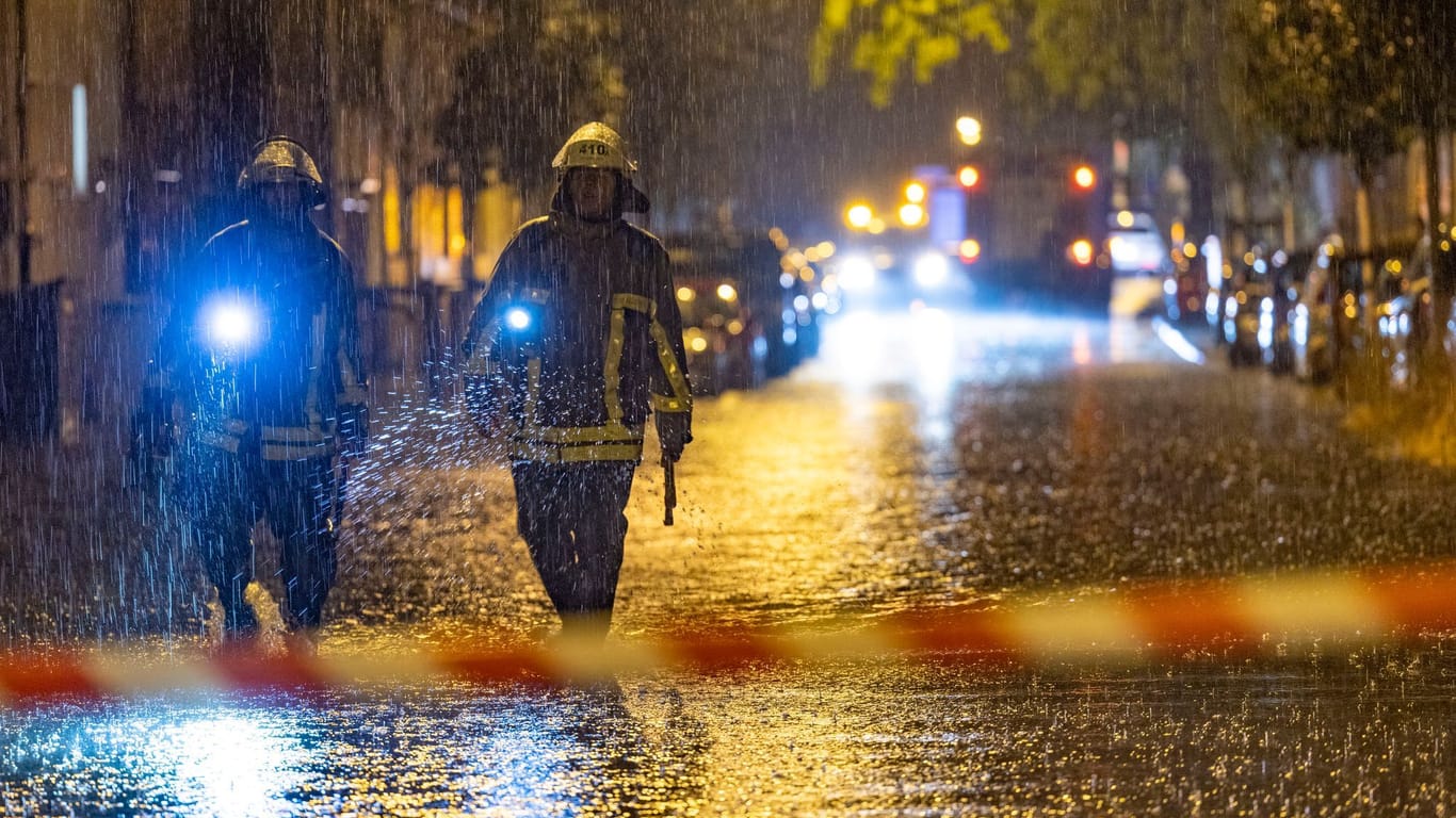 Feuerwehrleute suchen auf einer überfluteten Straße in Duisburg nach Gullydeckeln.